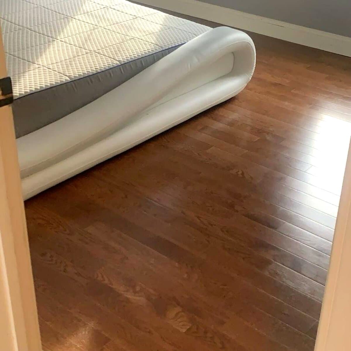 Warm brown hardwood boards extending through a bedroom doorway beside a white upholstered bed
