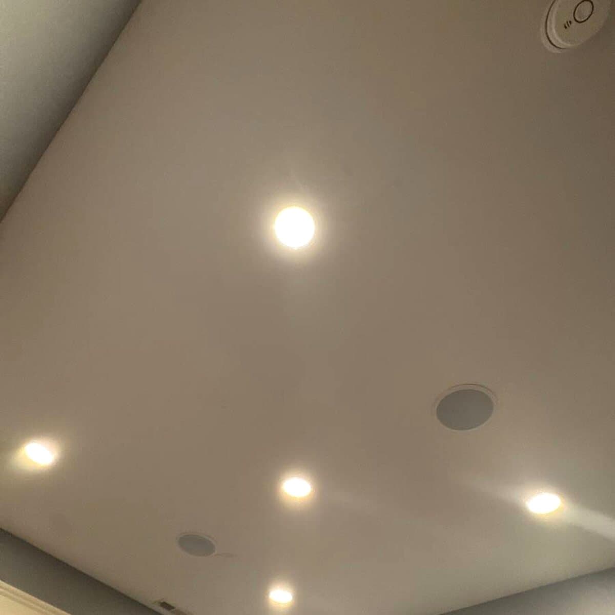 Recessed lights and round in-ceiling speaker grilles arranged across a pale ceiling