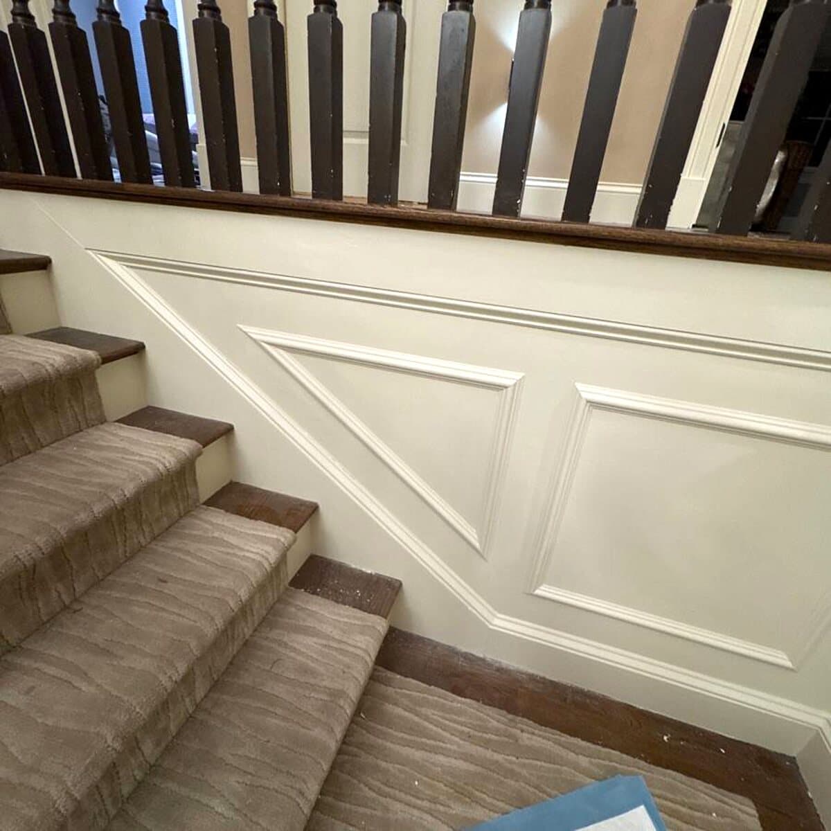 White picture-frame wainscoting following a staircase beneath dark wood balusters and a handrail